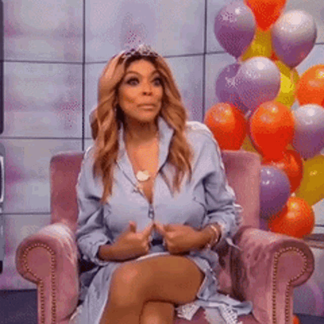 a woman wearing a tiara is sitting in a chair with balloons in the background .