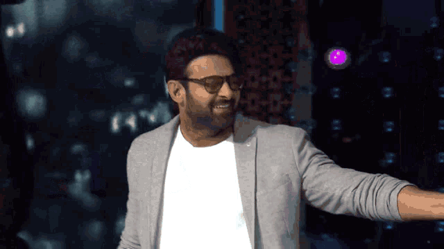 a man wearing glasses and a gray jacket is standing in front of a purple light