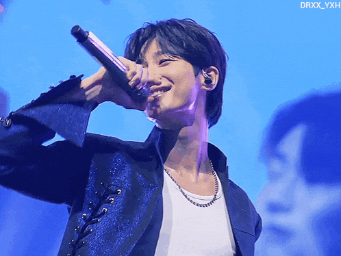 a man in a blue jacket is singing into a microphone with the name drxx_yxh on the bottom