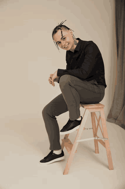 a man with dreadlocks sits on a wooden ladder