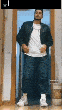 a man is standing in a doorway wearing a black jacket and a white t-shirt .