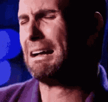 a man with a beard is crying with his eyes closed and a purple shirt on .