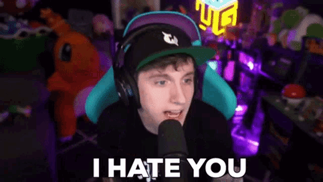 a man wearing headphones and a hat is sitting in front of a microphone and saying i hate you .