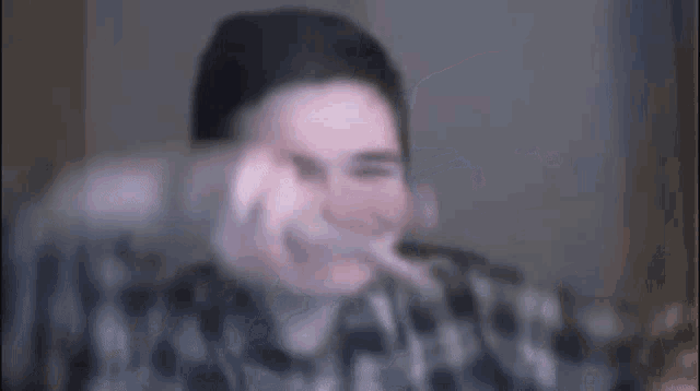 a man in a plaid shirt is making a funny face while sitting in front of a computer screen .