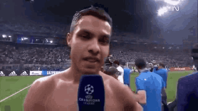 a shirtless man is talking into a champions league microphone on a soccer field .