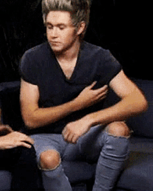 a young man is sitting on a couch with his hand on his chest .