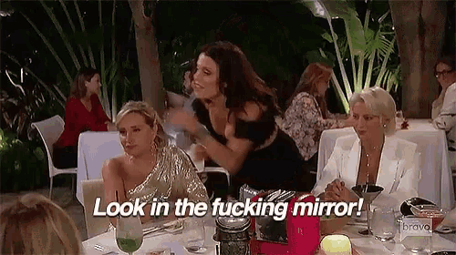 a group of women are sitting at a table and one of them is saying look in the fucking mirror