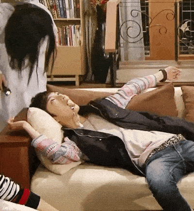 a man is laying on a couch in a living room with a woman standing behind him .