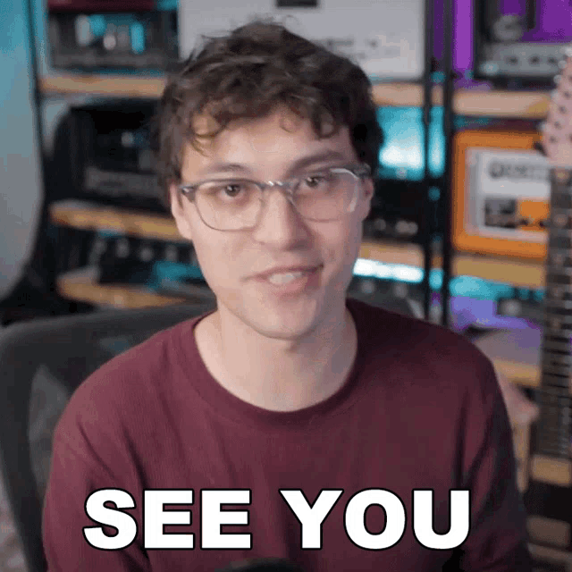 a man wearing glasses says see you in front of a guitar
