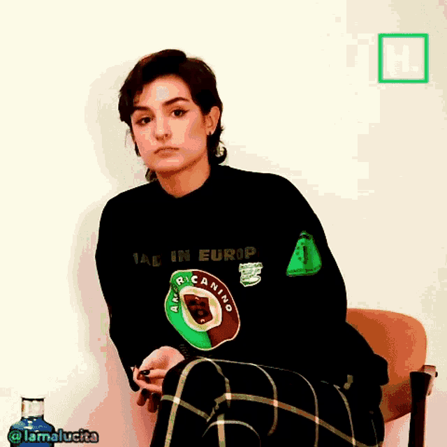 a woman wearing a black sweater and plaid pants is sitting in a chair with her legs crossed .