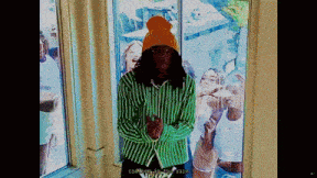 a man wearing a green and white striped shirt and an orange beanie stands in front of a window