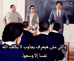 a man in a suit and tie is standing in front of a blackboard with arabic writing on it