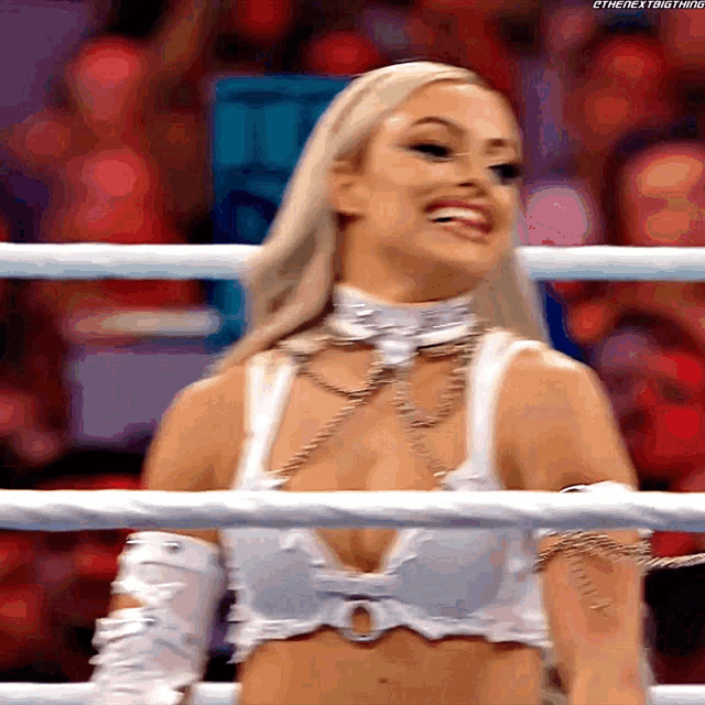 a woman in a white top is standing in a boxing ring smiling .