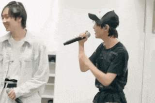 two men are singing into microphones in a room .