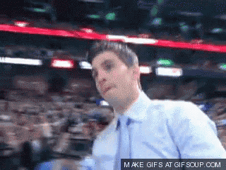 a man in a blue shirt and tie stands in front of a crowd with a make gifs at gifsoup.com link