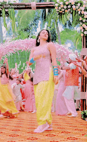 a woman in a pink top and yellow pants is dancing in front of a group of people .