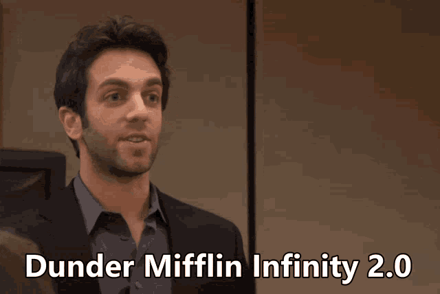 a man in a suit giving a peace sign with the words dunder mifflin infinity 2.0 below him