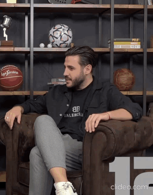 a man wearing a black shirt that says balenciaga sits on a couch