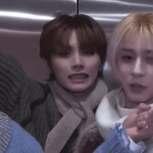 a man with a scarf around his neck is sitting next to another man in a blue sweater