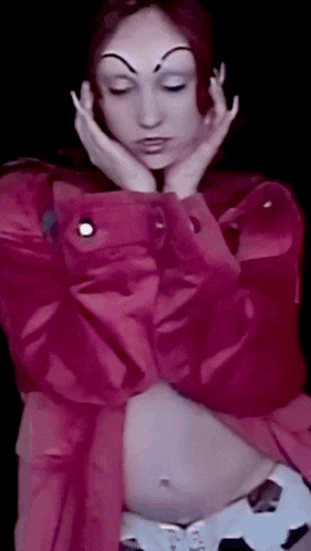 a woman in a pink jacket has her eyes closed and her hands on her face