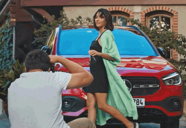 a man is taking a picture of a woman in front of a red mercedes with a license plate that says 784