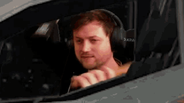 a man wearing headphones is driving a car and looking out the window .