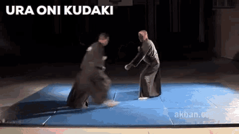 two men are fighting on a blue mat with the words ura oni kudaki written above them