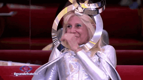 a woman is wearing a silver costume and covering her mouth with her hand .
