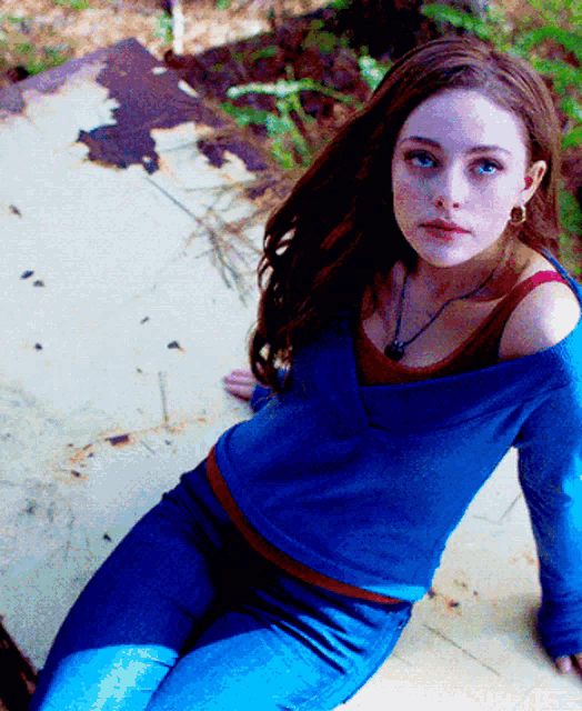 a woman wearing a blue sweater and blue jeans sits on a white surface