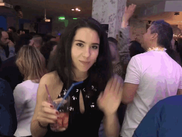 a woman in a black dress is holding a drink with a blue straw