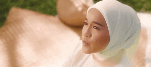 a woman wearing a hijab is sitting on a picnic blanket .