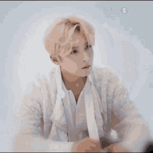 a young man with blonde hair is wearing a white shirt with ruffles and looking up .