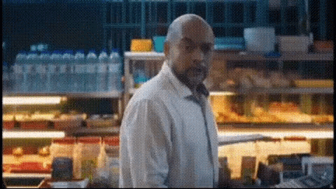 a man in a white coat is standing in front of a display case with bottles of water in the background .