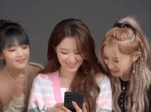 three girls are looking at a cell phone together and smiling