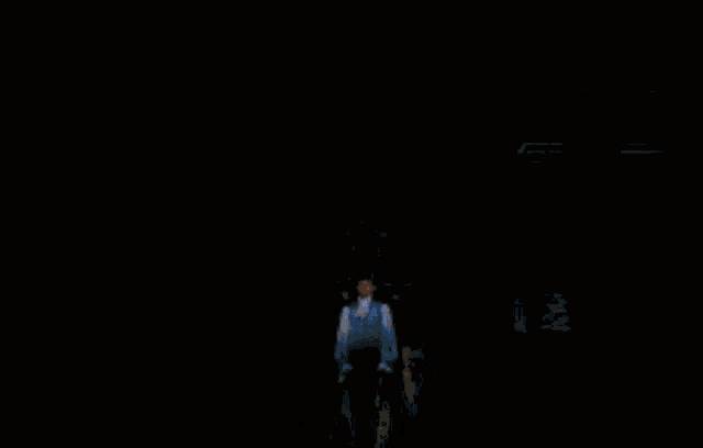 a man in a white shirt stands in a dark room with a light shining on him