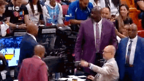 a man in a purple suit and tie is shaking hands with a man in a pink shirt .