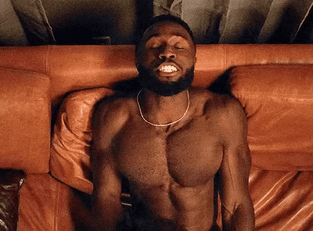 a shirtless man is laying on a brown leather couch with his eyes closed