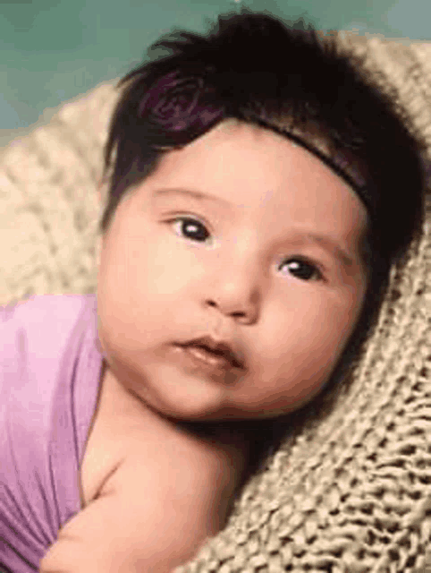 a baby girl wearing a purple headband is laying in a knitted basket .