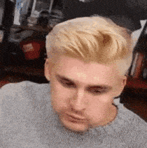 a man with blonde hair is wearing a gray sweater .