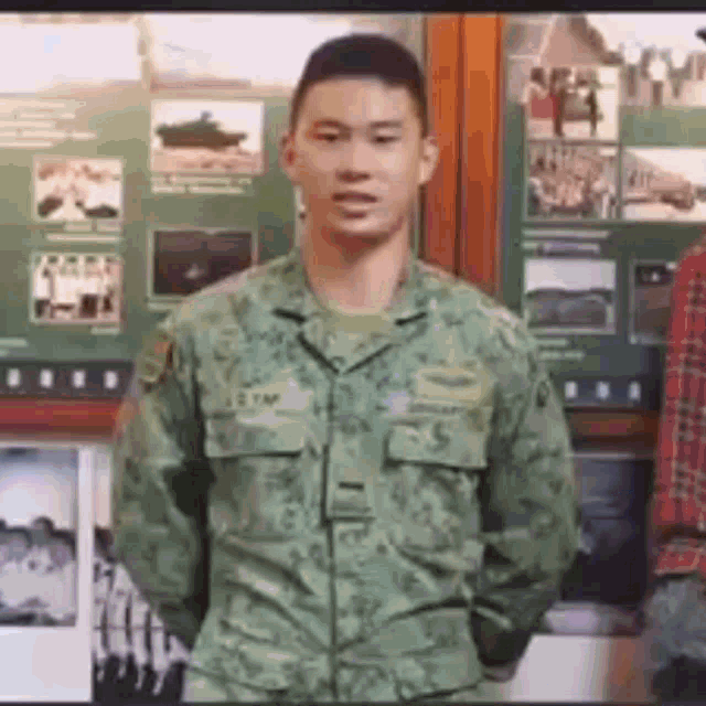 a man in a military uniform is standing in front of a wall with pictures of soldiers on it .