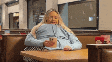 a woman is sitting at a table in a diner using her phone .