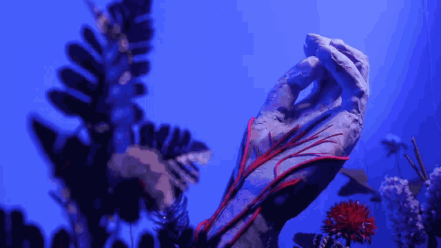 a statue of a hand with red veins and flowers in the background