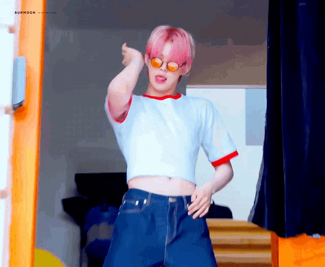 a man with pink hair is wearing a white crop top and blue shorts
