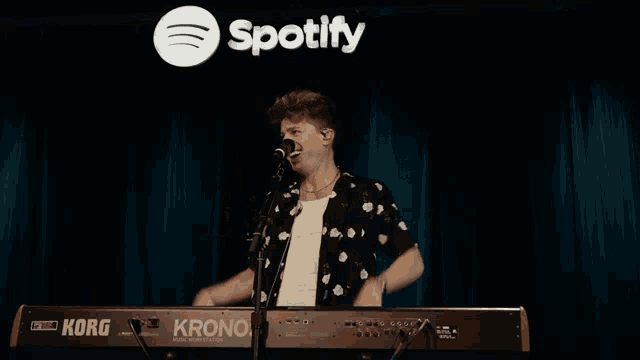 a man is singing into a korg keyboard in front of a spotify logo