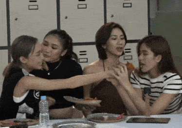 a group of women are sitting at a table with plates of food and a water bottle