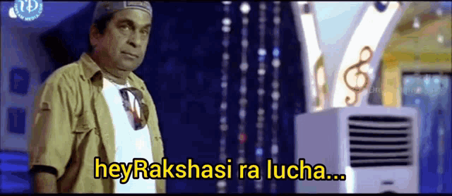 a man in a hat is standing in front of an air conditioner with the words hey rakshashi ra lucha written on it .