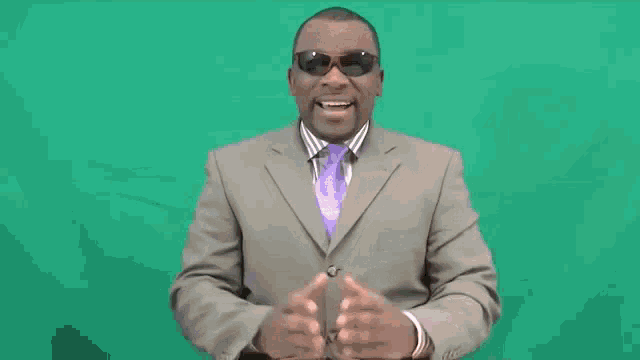 a man in a suit and tie is wearing sunglasses and making a hand gesture .