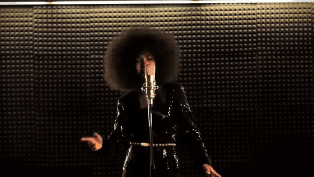 a woman singing into a microphone with a big afro