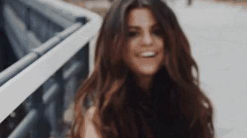 a woman with long hair is smiling and looking at the camera while standing on a sidewalk .