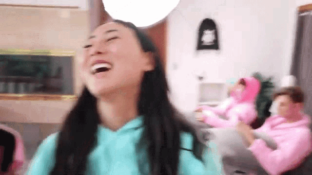 a woman in a blue hoodie is laughing while sitting on a couch in a living room .